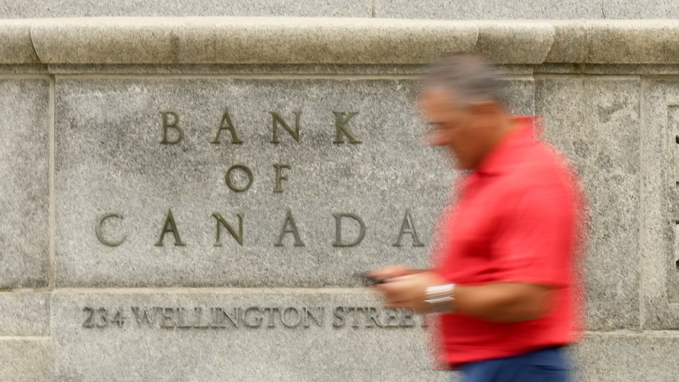 A man checks his phone as he walks past the Bank of Canada building in Ottawa